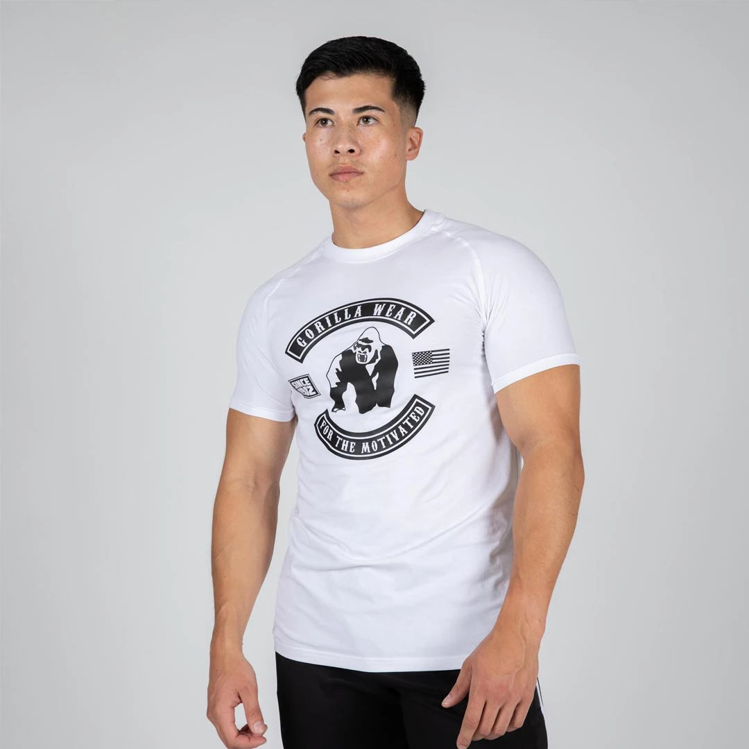 Man i Gorilla Wear Tulsa T-Shirt White, en vit kroppsnära tränings-t-shirt med stort svart logotryck., bild 2 av 3