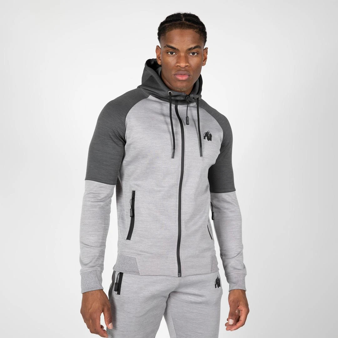 Man i Gorilla Wear Sullivan Track Jacket Grey, en grå träningsjacka med dragkedja, huva och mörkgrå axelpartier., bild 1 av 7
