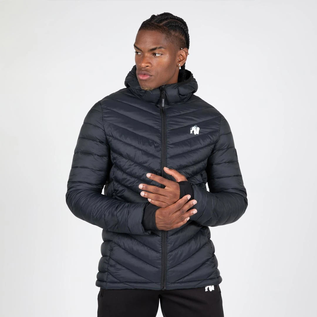 Gorilla Wear Osborn Puffer Jacket Black, en svart vadderad jacka med huva och tumhål buren av en manlig modell., bild 2 av 8