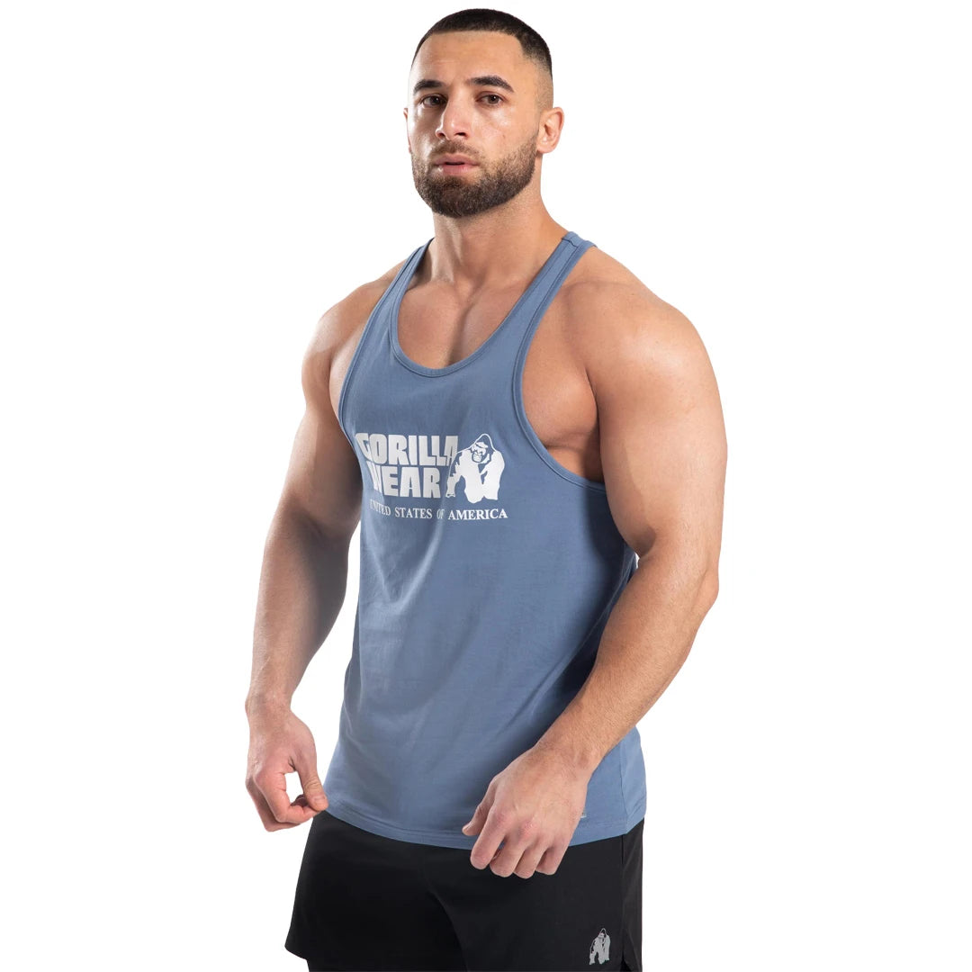 Gorilla Wear Classic Tank Top Coronet Blue är ett blått brottarlinne i bomull med vitt tryck, här buret av en man., bild 6 av 7