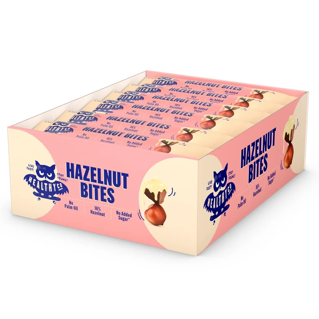 18 x HealthyCo Hazelnut Bites 21 g i en ljusgul och rosa displaylåda fylld med matchande chokladbitar.