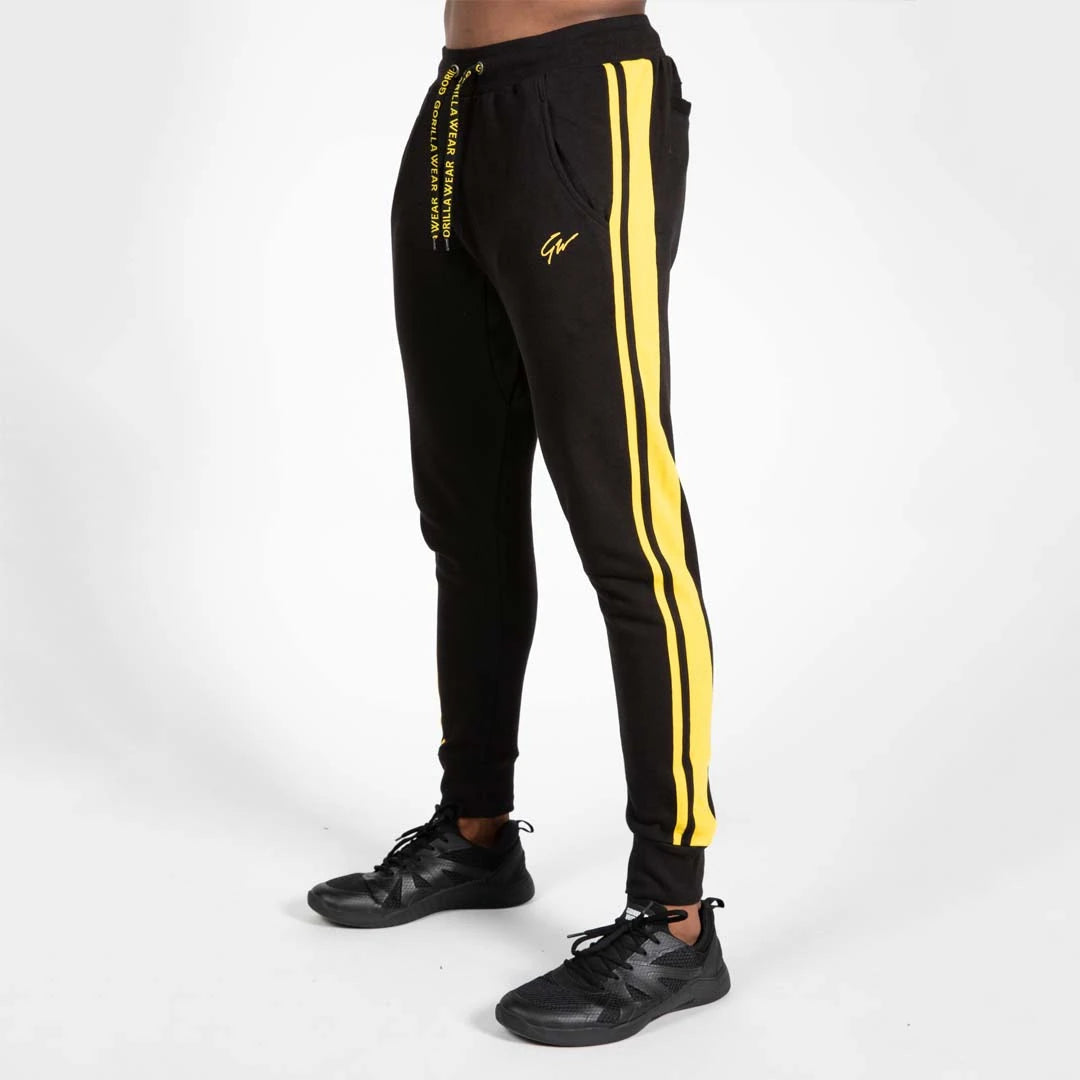 Svarta Gorilla Wear Banks Pants Black/Yellow träningsbyxor med gula sidostripar, fickor och dekorerade snören.