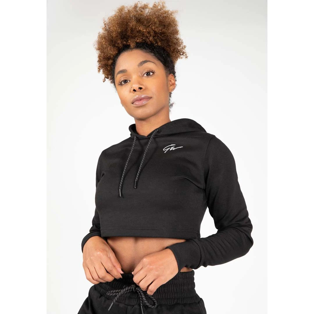 Gorilla Wear Pixley Crop Top Hoodie Black, en svart croppad huvtröja i slim fit med dragsko, buren av en kvinna.