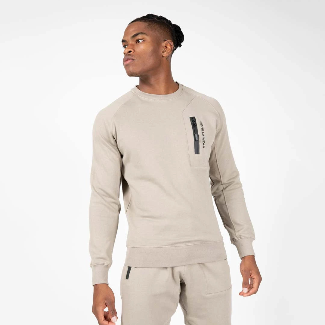 Manlig modell bär Gorilla Wear Newark Sweater Beige, en avslappnad bomullströja med svart bröstficka och dragkedja., bild 1 av 1